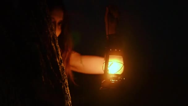 Scary woman with a lantern in night scene - Τρομακτική εικόνα μιας τρομακτικής γυναίκας με σκούρα μάτια και εμφάνιση μάγισσας, με λευκό φόρεμα, κρατώντας αναμμένο φανάρι, σε σκοτεινή νυχτερινή ατμόσφαιρα. - Πλάνα, βίντεο