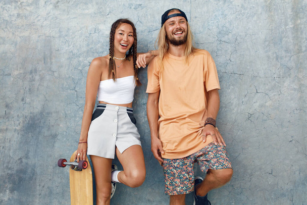 Couple With Skateboards Portrait. Happy Guy And Girl In Casual Outfit Against Concrete Wall At Skatepark. Urban Subculture And Skateboarding As Lifestyle Of Active People In City. - 写真・画像