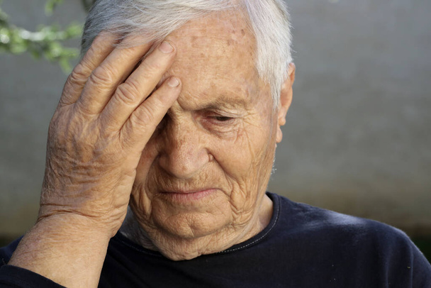 Старшая белая женщина держит руку на лбу. Головная боль, депрессия или симптомы болезни Альцгеймера. - Фото, изображение