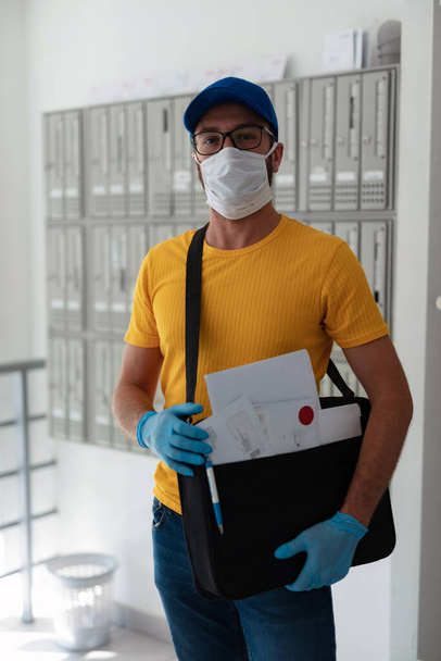 Un facteur livre du courrier avec un sac postal, un masque de protection et des gants pendant une pandémie de virus. - Photo, image