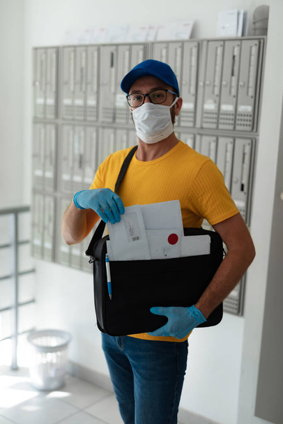 Briefträger, der während einer Virenpandemie Post mit Brieftasche und Schutzmaske und Handschuhen zustellt. - Foto, Bild