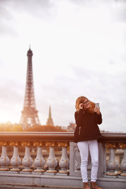 Девушка с мобильным телефоном на фоне Парижа, реки Сены и Эйфелевой башни. - Фото, изображение