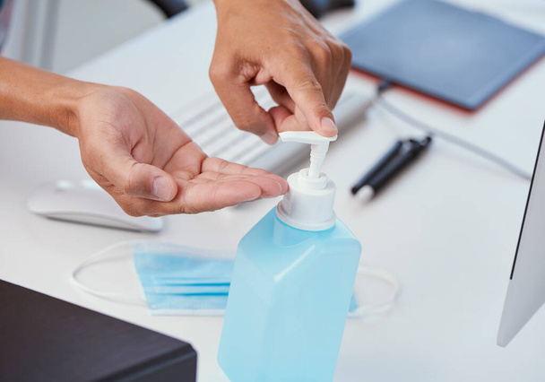 primer plano de un joven caucásico en su escritorio de la oficina desinfectando sus manos con desinfectante de manos de una botella azul - Foto, Imagen