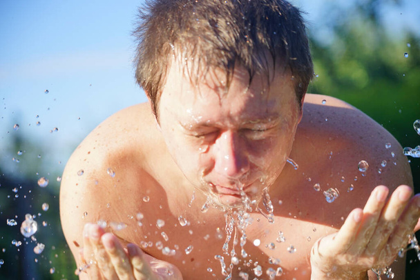 de man wast zich met koud water in de tuin - Foto, afbeelding