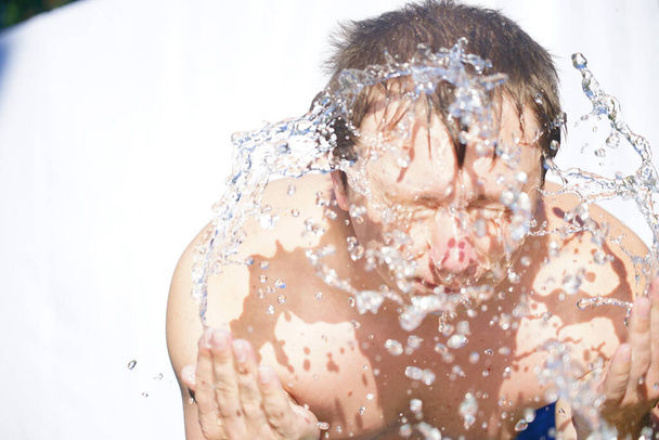The guy washes his face with water, drops fly in different directions, on a white background - Foto, afbeelding