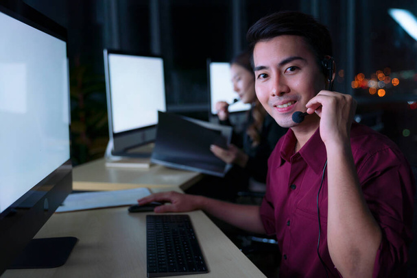 Thai Asian man customer services care operators working night shift in call center for helping assistance client in workplace at night time, Friendly helpdesk operator working at night - Photo, Image