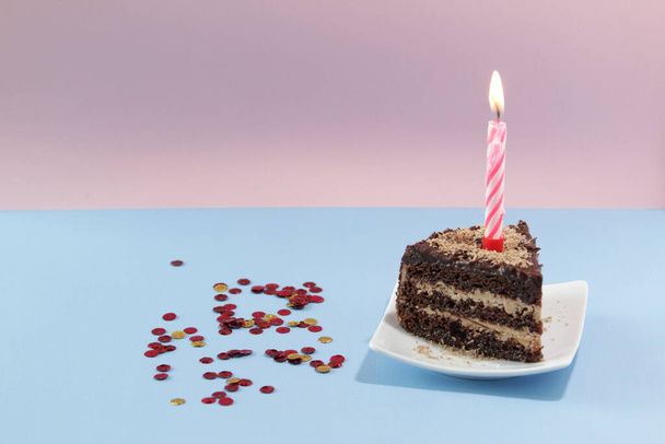 Slice of Birthday Cake with a candle and confetti on a blue background.  - Foto, Bild
