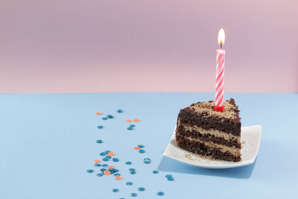Slice of Birthday Cake with a candle and confetti on a blue background.  - Foto, Imagen
