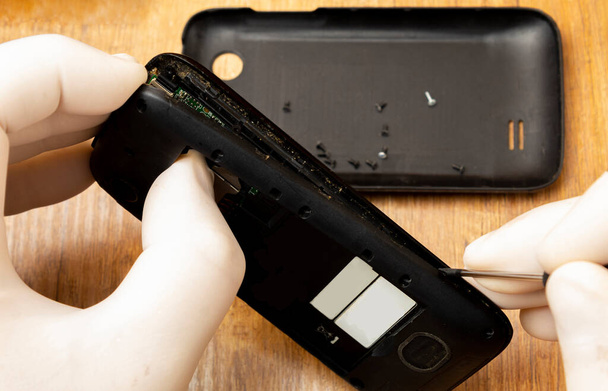 Demontage eines alten Telefons mit einem Schraubenzieher zur Reparatur und Reinigung. - Foto, Bild