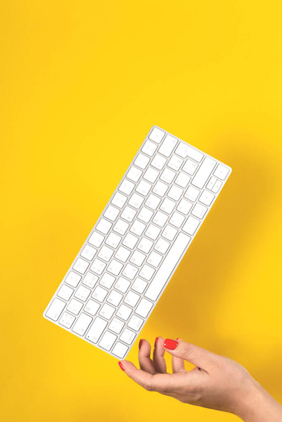 Keyboard balances on womans hand on yellow background - Photo, Image