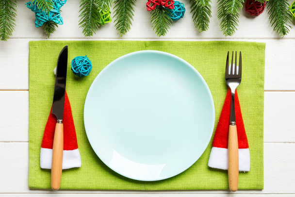 Çatal, bıçak ve tabağın üst görüntüsü köknar ağacı ve ahşap arka planda Noel süslemeleri ile çevrili. Yeni yıl arifesi ve tatil yemeği konsepti. - Fotoğraf, Görsel