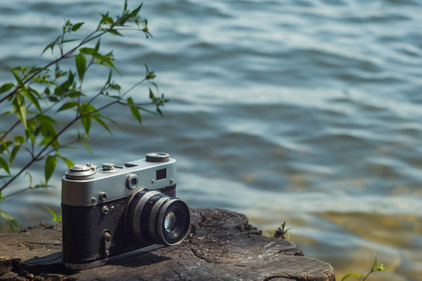 Vintage analog camera lies on the stump next to the water. Background. - Photo, Image