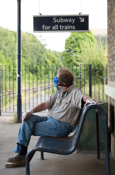 Хэмпшир, Англия, Великобритания. 2020 год. Мужчина, путешествующий по железной дороге в медицинском защитном снаряжении, маске, очках и перчатках во время вспышки Ковид-19, ждет на платформе поезда. - Фото, изображение