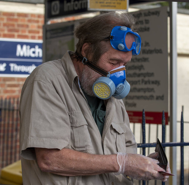 Hampshire, Anglia, Egyesült Királyság. 2020. Egy férfi vasúti utazó, aki orvosi védőfelszerelést, maszkot, szemüveget és kesztyűt viselt a Covid-19-es járvány idején, ellenőrizte a pénztárcáját, miután jegyet vett az utazásra.. - Fotó, kép