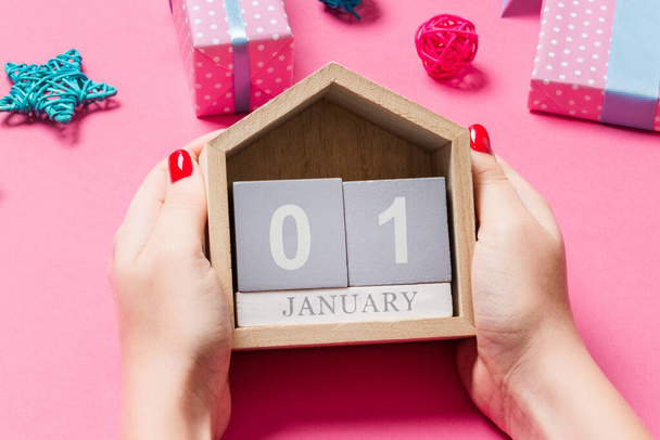 Top view of female hands holding calendar on pink background. The first of January. Holiday decorations. New Year concept. - Photo, Image