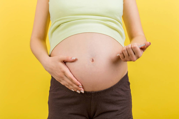 Zugeschnittenes Bild einer schwangeren Frau, die Insulin spritzt, um den Zuckerspiegel auf farbigem Hintergrund mit Kopierraum zu kontrollieren. Gesundheitskonzept. - Foto, Bild