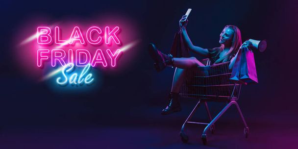 Portrait of young woman in neon light on dark backgound. The human emotions, black friday, cyber monday, purchases, sales, finance concept. Neoned lettering. - Foto, afbeelding