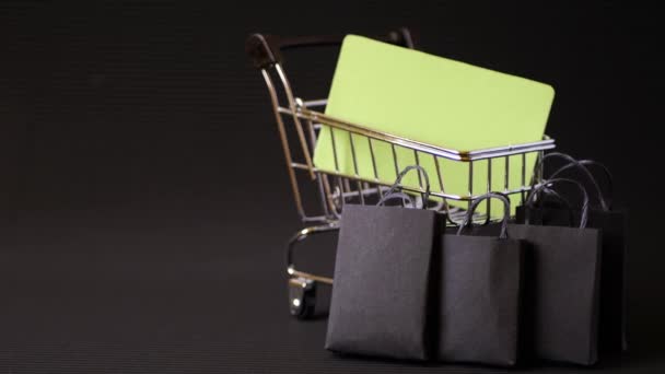 Shopping cart or trolley with paper bags on black background. Credit card mock up. Online store purchases. Black background. Minimalism design. Black friday promotion. Final sale - Footage, Video
