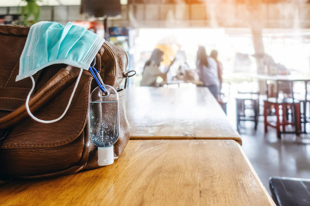 Mini portable alcohol gel bottle to kill Corona Virus(Covid-19) hang on a leather shoulder bag of a woman on table at cafeteria. New normal lifestyle.Selective focus on alcohol gel - Foto, imagen