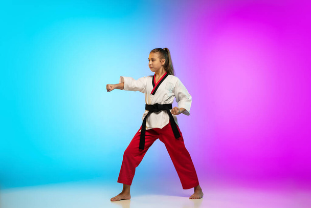 Karate, taekwondo girl with black belt isolated on gradient background in neon light - Zdjęcie, obraz