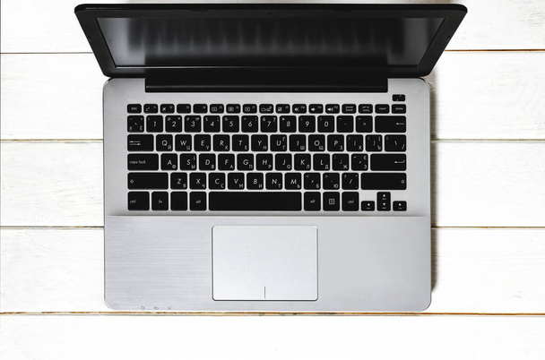 Grey laptop with black keyboard stands on white wood table. top view - Fotoğraf, Görsel