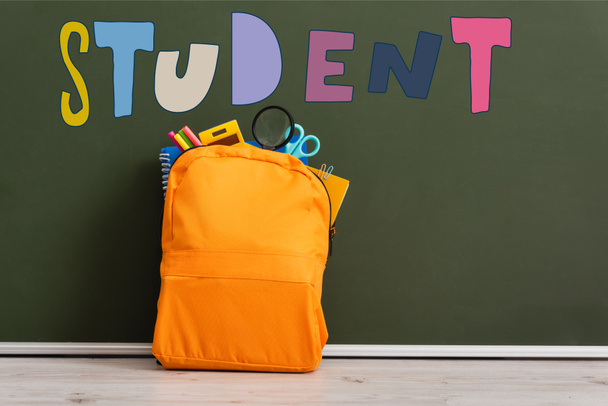 mochila amarilla llena de papelería escolar cerca de pizarra verde con letras de estudiante  - Foto, imagen