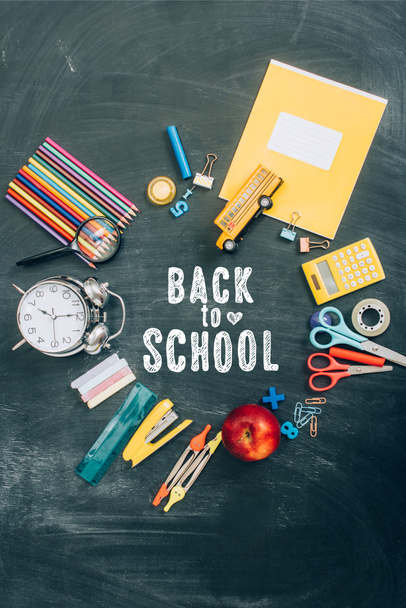 bovenaanzicht van frame met vintage wekker, groene appel en schoolbenodigdheden op zwart schoolbord met terug naar school belettering  - Foto, afbeelding