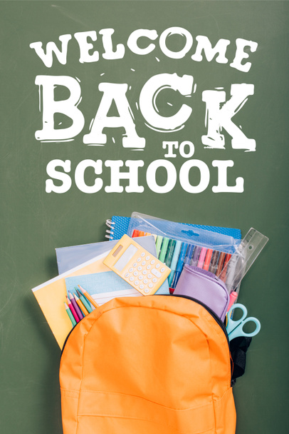 vista superior de la mochila llena de papelería escolar en pizarra verde con bienvenida de nuevo a las letras de la escuela  - Foto, imagen