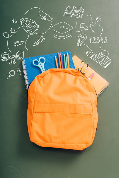 top view of backpack packed with school stationery on green chalkboard with illustration  - Photo, Image