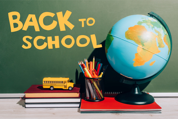 globe and pen holder on notebook near toy school bus on books near green chalkboard with back to school lettering  - Photo, Image