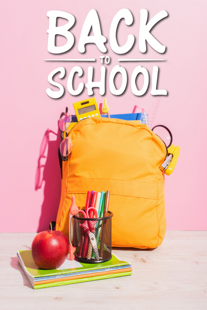 packed school backpack near notebooks, pen holder with felt pens and scissors, ripe apple and beck to school lettering on pink - Photo, Image
