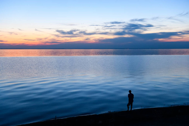 Μοναχική σιλουέτα ενός άντρα που στέκεται δίπλα στη θάλασσα το ηλιοβασίλεμα. Υψηλής ποιότητας φωτογραφία - Φωτογραφία, εικόνα