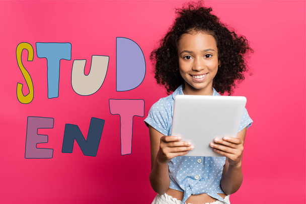 curly african american kid using digital tablet near student lettering on pink - Fotó, kép