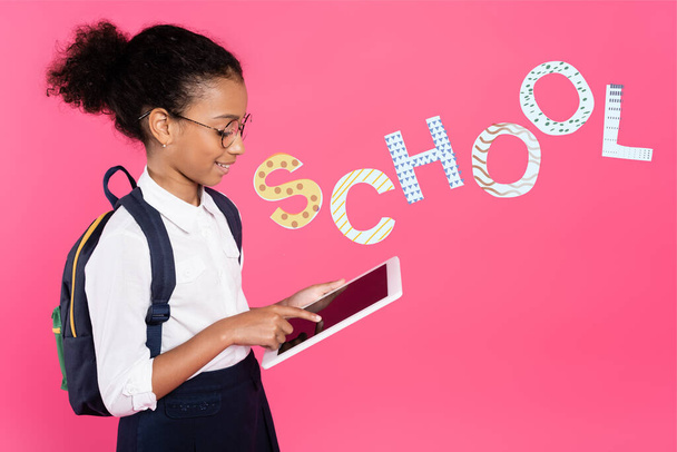 afro-americana estudante em óculos com mochila usando tablet digital perto da escola lettering em rosa - Foto, Imagem