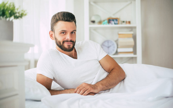 Close up photo of handsome young bearded man lying in bed and relaxing on the morning - Valokuva, kuva