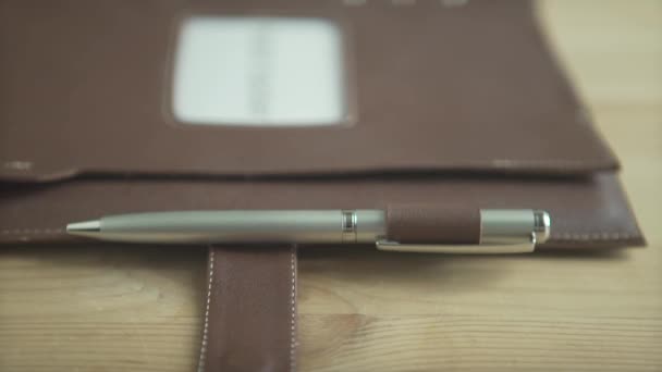 Όμορφο κοντινό πλάνο από ανοιχτό καφέ δερμάτινο σημειωματάριο σφαίρα σημειωματάριο βιβλίο με ασημένια θήκη στυλό στο ξύλινο τραπέζι - Πλάνα, βίντεο