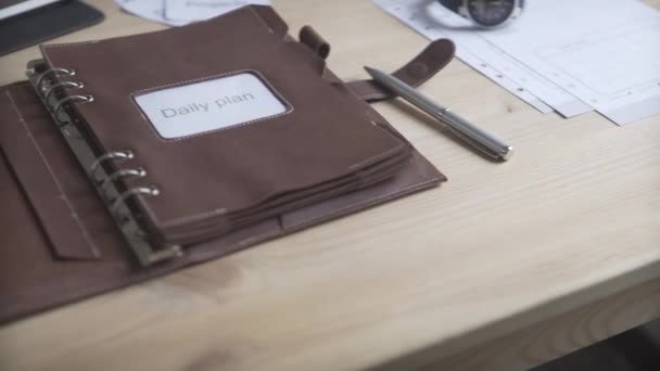 Primer plano plano del elegante estuche de cuero marrón claro libreta de notas planificador diario bala diario hábito rastreador en la mesa de madera - Metraje, vídeo