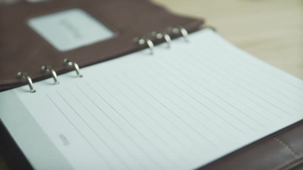 Közelkép barna bőr jegyzetfüzet könyv üzleti projekt napi tervező golyó napló szokás nyomkövető fa asztalon - Felvétel, videó