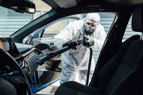 Mężczyzna w ŚOI dezynfekujący wnętrze samochodu z COVID-19 chemikaliami - Zdjęcie, obraz