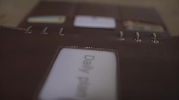 Hermoso primer plano de cuero marrón titular de la tarjeta cubierta organizador diario planificador diario bloc de notas sobre tabla de madera - Metraje, vídeo