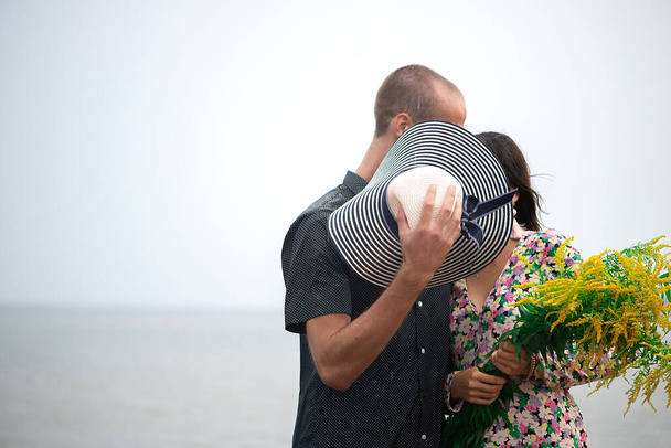 Jeune couple romantique baisers et câlins, cacher leurs visages derrière leurs chapeaux d'été - Photo, image