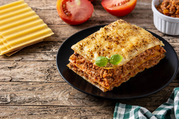 Piece of meat lasagna on black plate on wooden table.Copy space - Foto, imagen