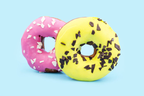 желтые и розовые пончики, украшенные кусочками шоколада на синем фоне. Крупный план. - Фото, изображение