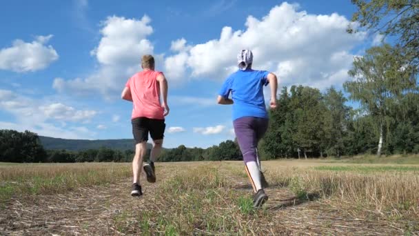 Guy en meisje rennen op het geoogste veld. Sport gezonde levensstijl. Lopende atleten genieten samen van hardlopen. Langzame beweging - Video