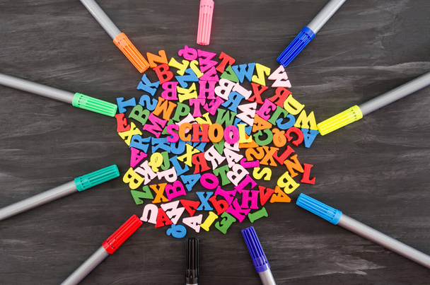 English colored letters and colored markers. School concept background. ... School supplies on a black wooden background. View from above. - Foto, Imagen