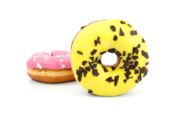 dos rosquillas dulces en esmalte rosa y amarillo y con chispas de chocolate aisladas sobre un fondo blanco. - Foto, imagen