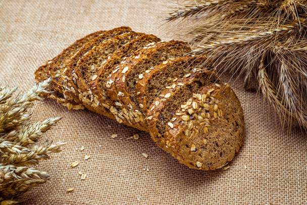 Προϊόντα αρτοποιίας. Ψωμί σίκαλης με τραγανά καρβέλια και ψίχουλα. Φρέσκο καρβέλι χωριάτικο παραδοσιακό ψωμί με στάρι σταριού στο αυτί ή φυτό ακίδα σε φυσικό βαμβακερό φόντο. Concept - Μαγειρική στο σπίτι - Φωτογραφία, εικόνα
