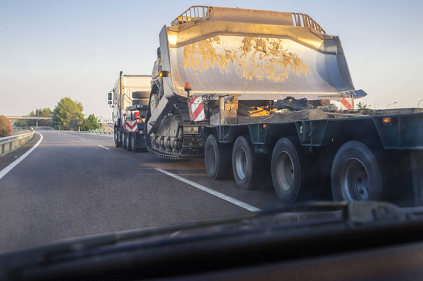 Ein überdimensionaler Lastkraftwagen transportiert eine riesige Baggermaschine. Blick aus dem Inneren des Autos - Foto, Bild