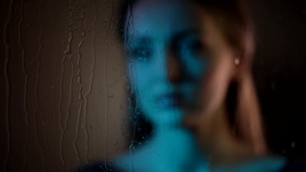 Sogno triste attraente giovane donna caucasica guarda la finestra di vetro fumante mano di palmo toccante nella luce blu notte al neon - Filmati, video
