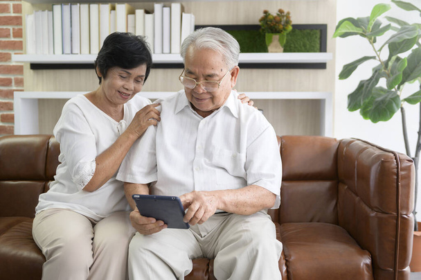 A happy senior Asian couple is using tablet and talking with family on webcam at home, retirement concept. - Foto, Imagem